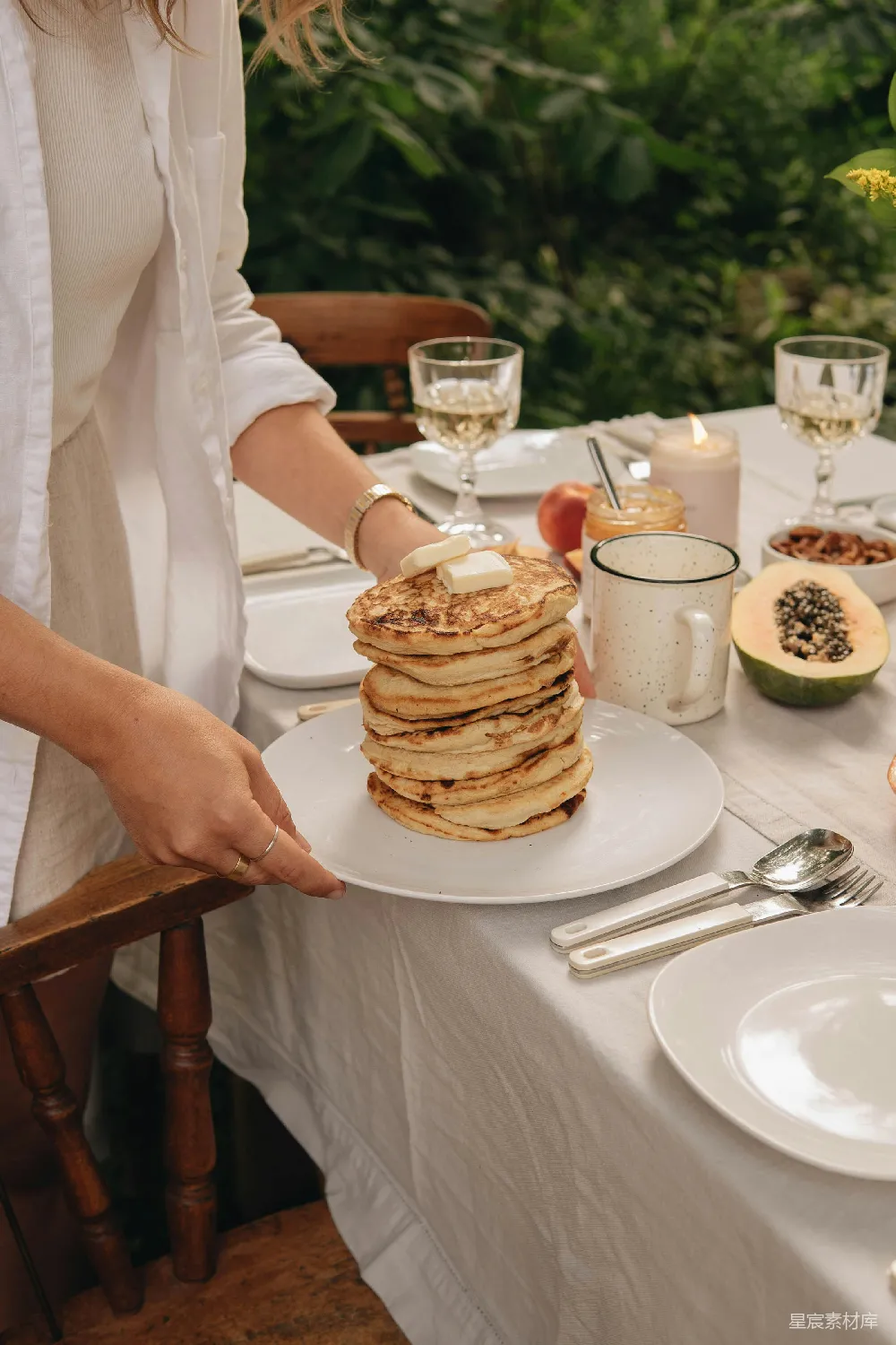 高清摄影 自然 白裙女子手持白色陶瓷盘子，盘中有 Pancakes。
