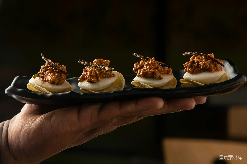 高清摄影  一只手拿着一个上面摆放着小 appetizer 的黑色盘子