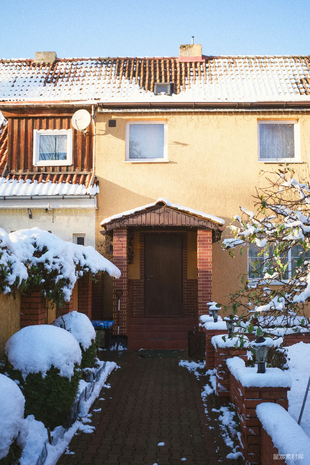 高清摄影  屋顶有雪、院子里有灌木丛的黄色房子。