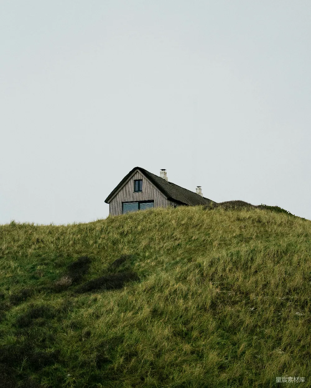 高清摄影  一座小屋坐落在草地上的一座小山上。