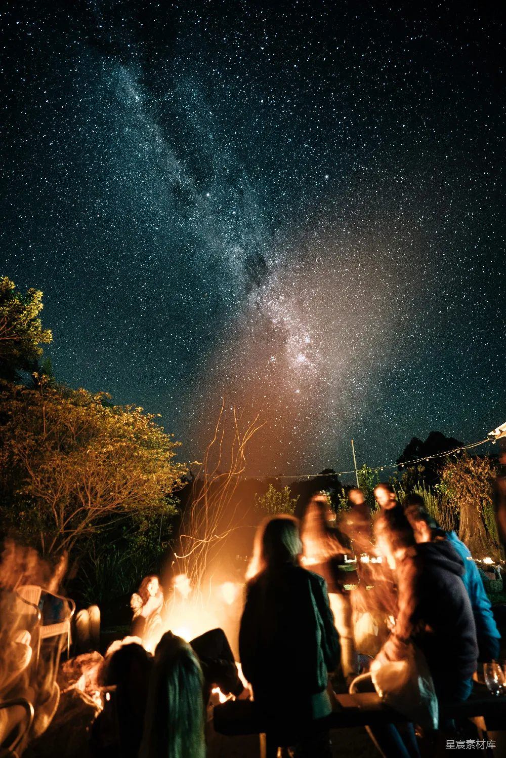 高清摄影  一群人围坐在篝火旁，夜空中满是星星。