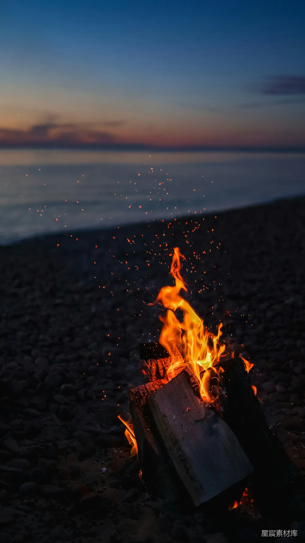 高清摄影  夕阳下，火光在棕色沙滩上燃起，靠近水边。