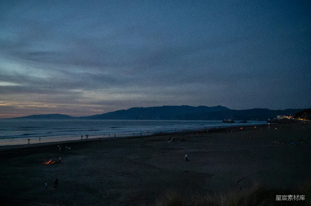 高清摄影  夕阳笼罩着一片广阔的海滩，远处是海洋和连绵的山脉。
