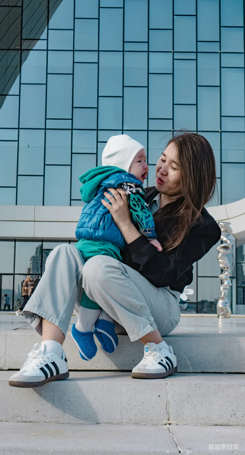 高清摄影  一位母亲抱着一个婴儿站在现代化的建筑前。
