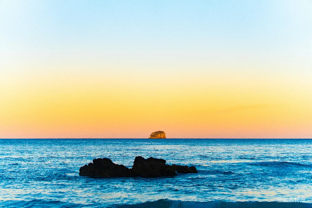 高清摄影 夕阳西下，海平线上有一块岩石在 foreground。