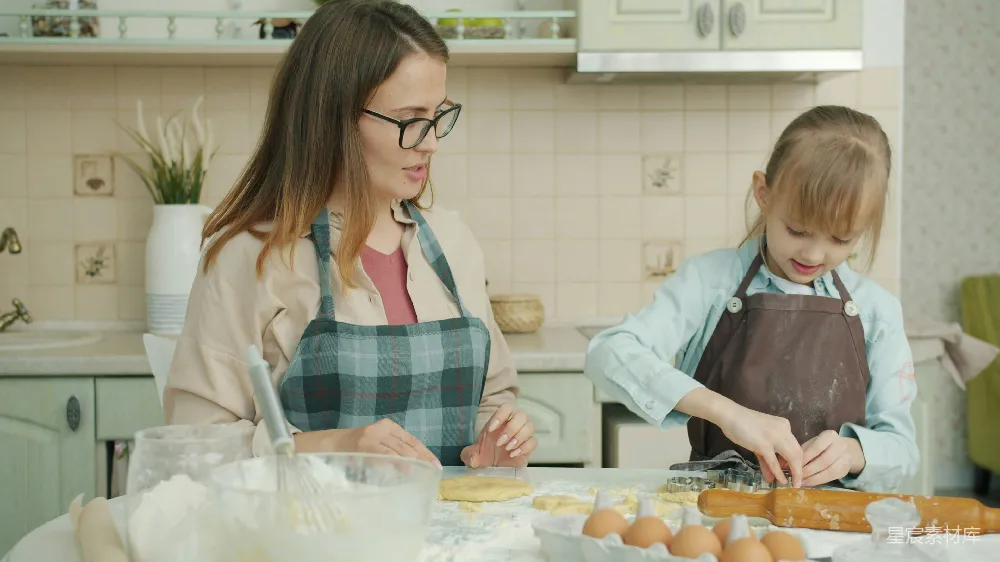 年轻女子和小女孩穿着围裙在厨房里做饼干并聊天，人们显得轻松愉快。这体现了家庭生活和母性的概念。