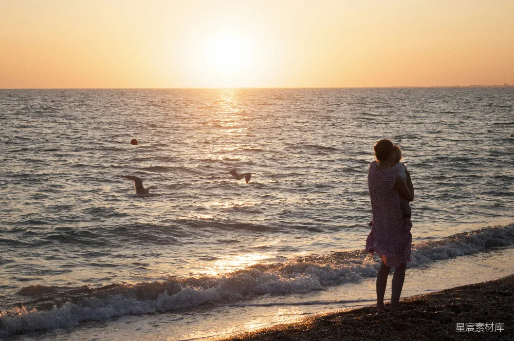 高清摄影  一位女士站在海滩上，看着夕阳落下。