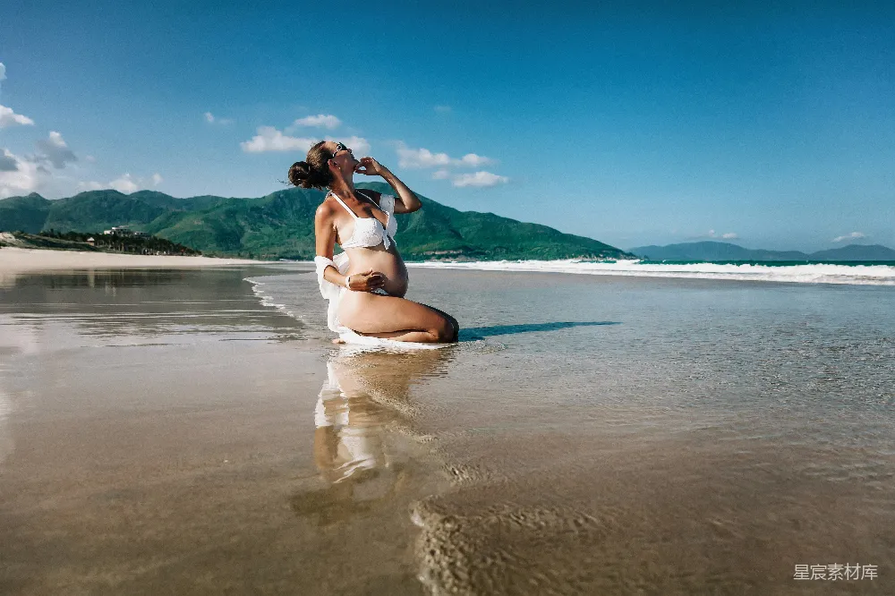 高清摄影  怀胎的女人站在潮湿的沙滩上摆姿势。