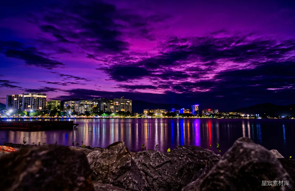 高清摄影  灰色的海岸岩石，在夜景中可以看到城市的天际线。