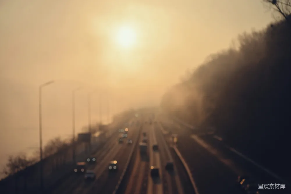 雾蒙蒙的高速公路上汽车在日出时分行驶。