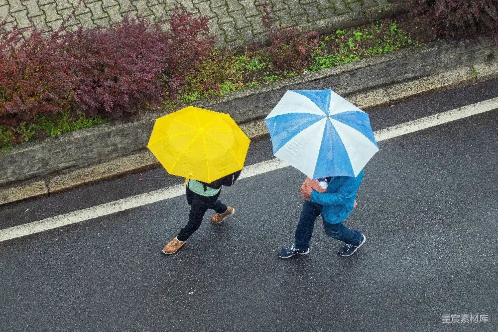 高清摄影  身穿蓝色牛仔裤的人手持黄色雨伞在人行道上行走，白天时间。