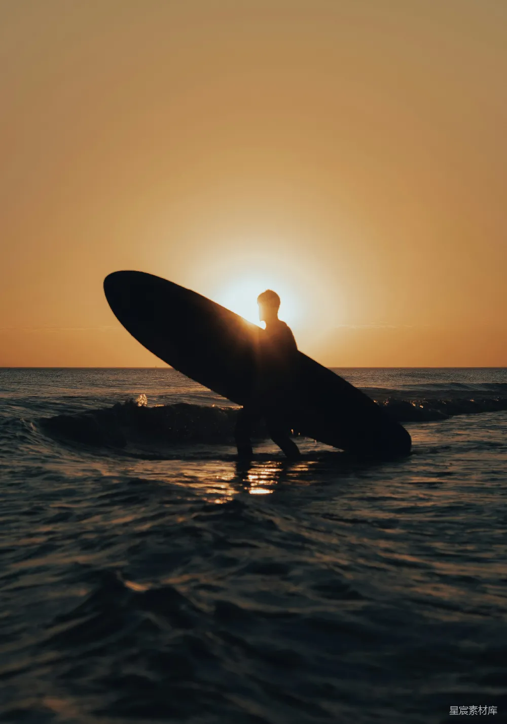 夕阳下，一个男子手持冲浪板在海边。