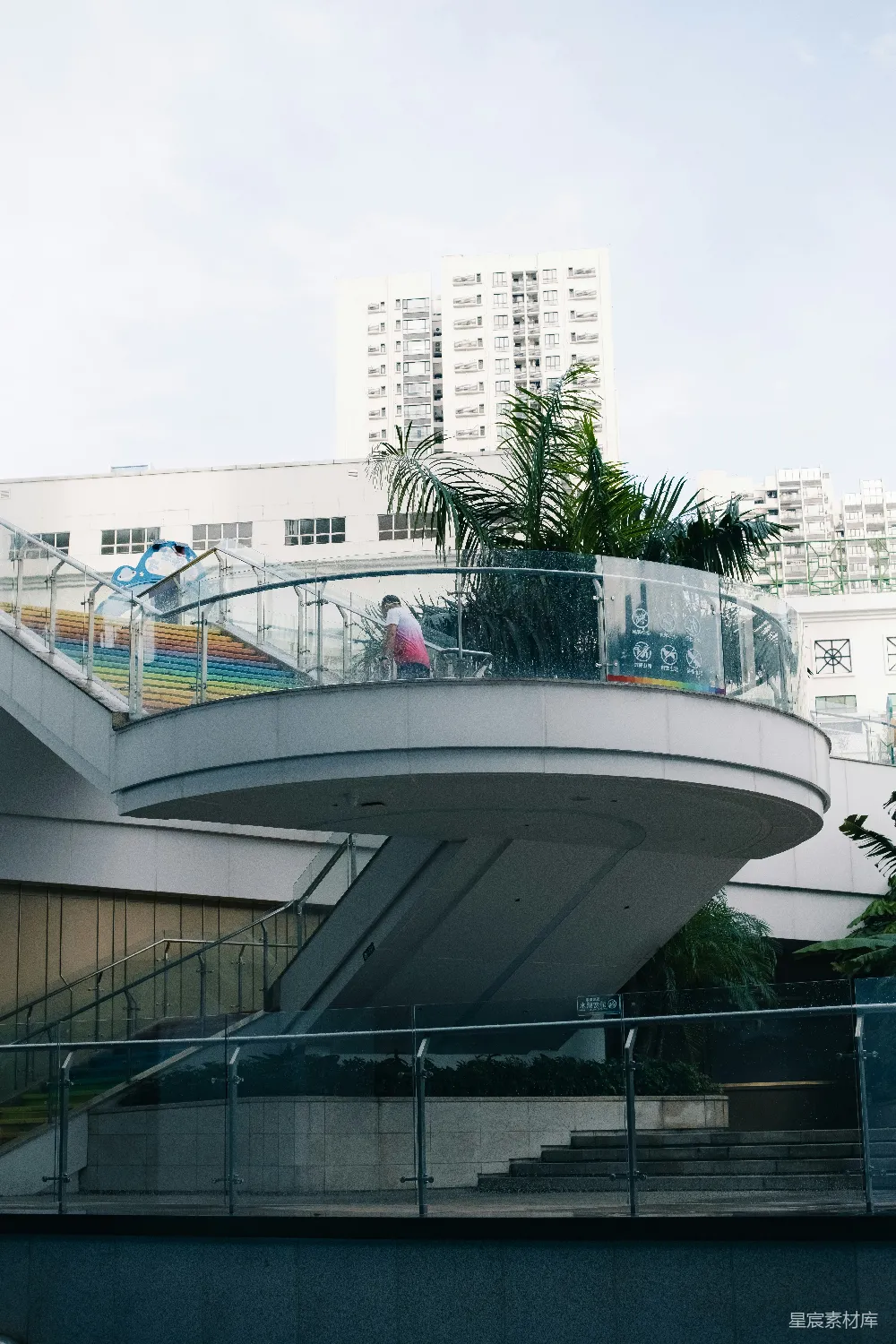 高清摄影  弯曲彩虹楼梯，有人在场，旁边是现代化建筑。