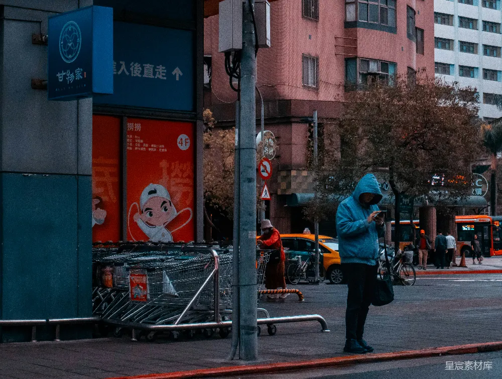 高清摄影  穿蓝色连帽衫的男人在城市街道上查看手机。