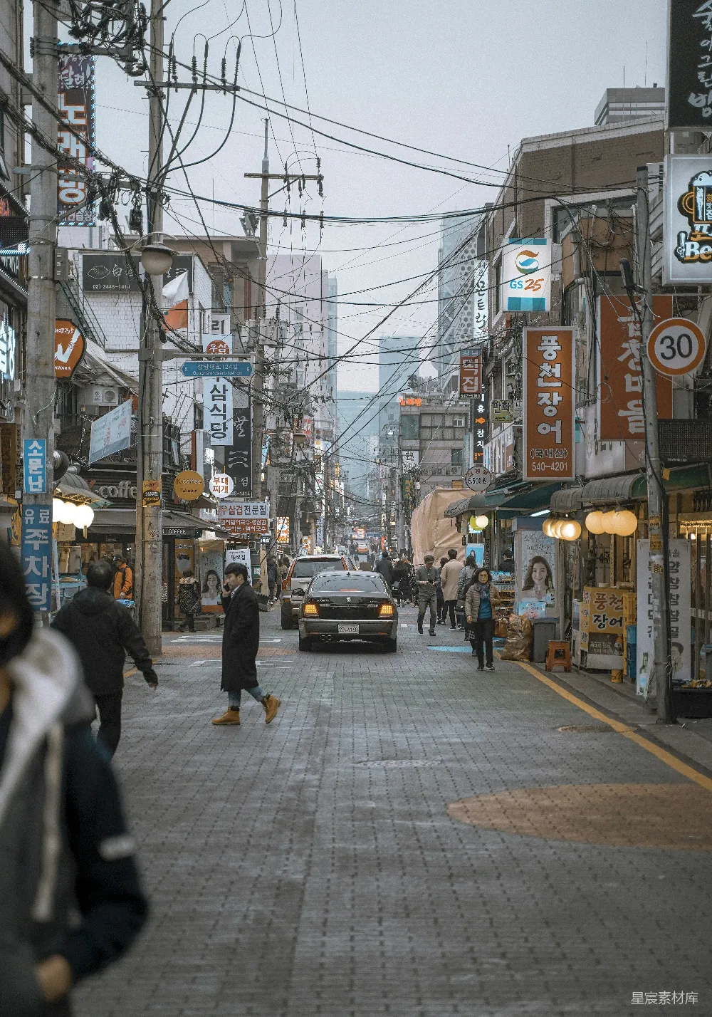高清摄影  人们在街道上行走，中间有两辆汽车。