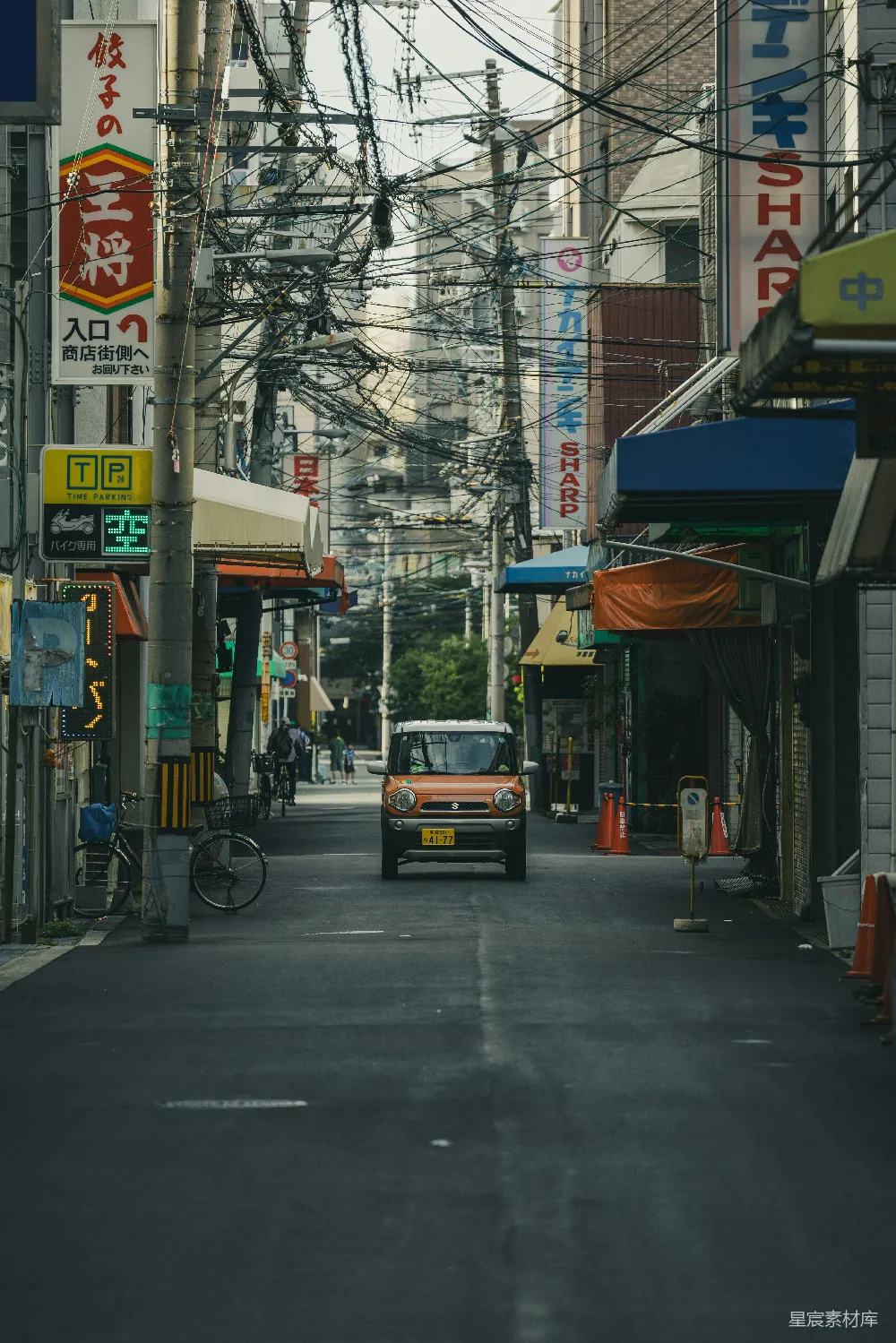 橙色小轿车在一条狭窄的城市街道上行驶。
