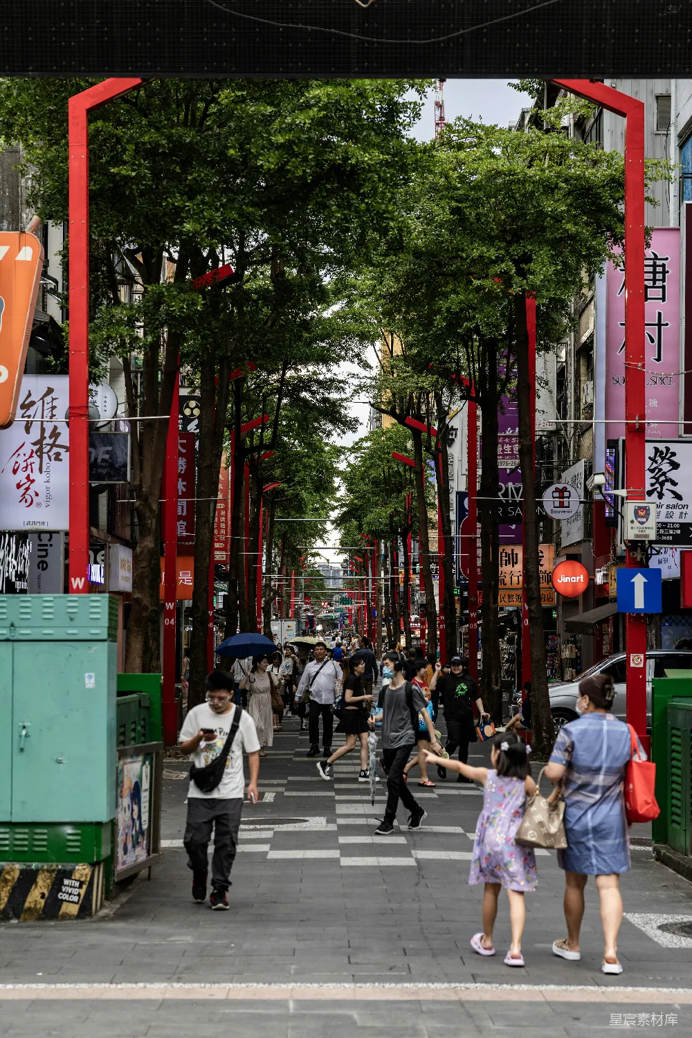 高清摄影  人们走在一条种满树木的街道上，街道上有红色的拱门。