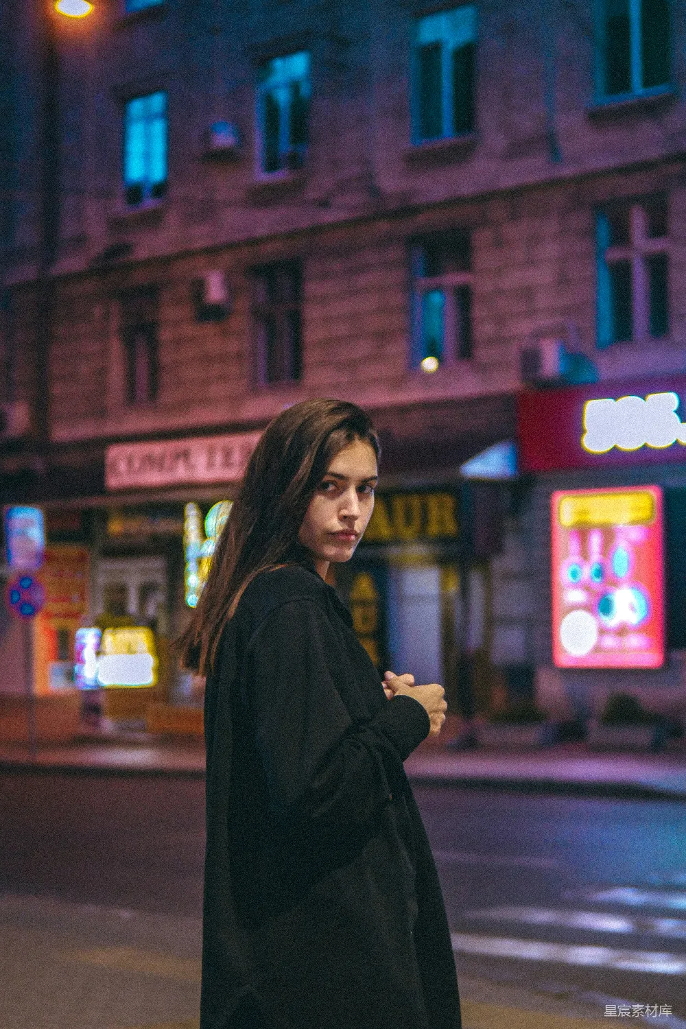 黑外套的女人站在红建筑附近的一个夜晚。