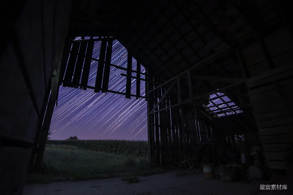 夜晚，长时间曝光下的星空映衬在一座棕色木屋上方。