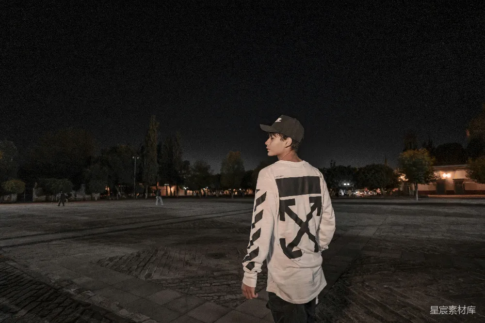 高清摄影  一个穿着Off-White长袖衬衫的男人在夜间站着。