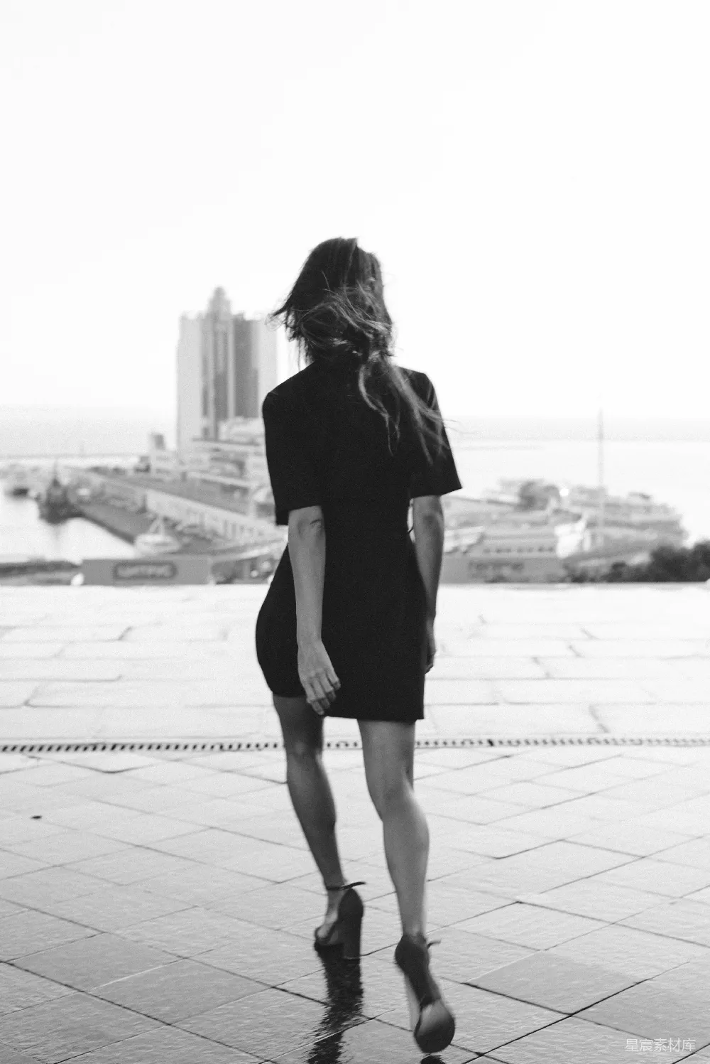 高清摄影  身穿黑裙的女子在白天的人行道上行走。