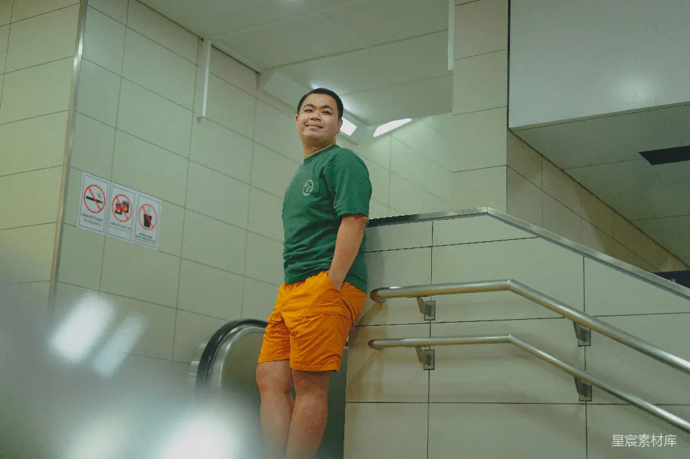 一个穿着绿色上衣和橙色短裤的男人站在电梯扶手上。