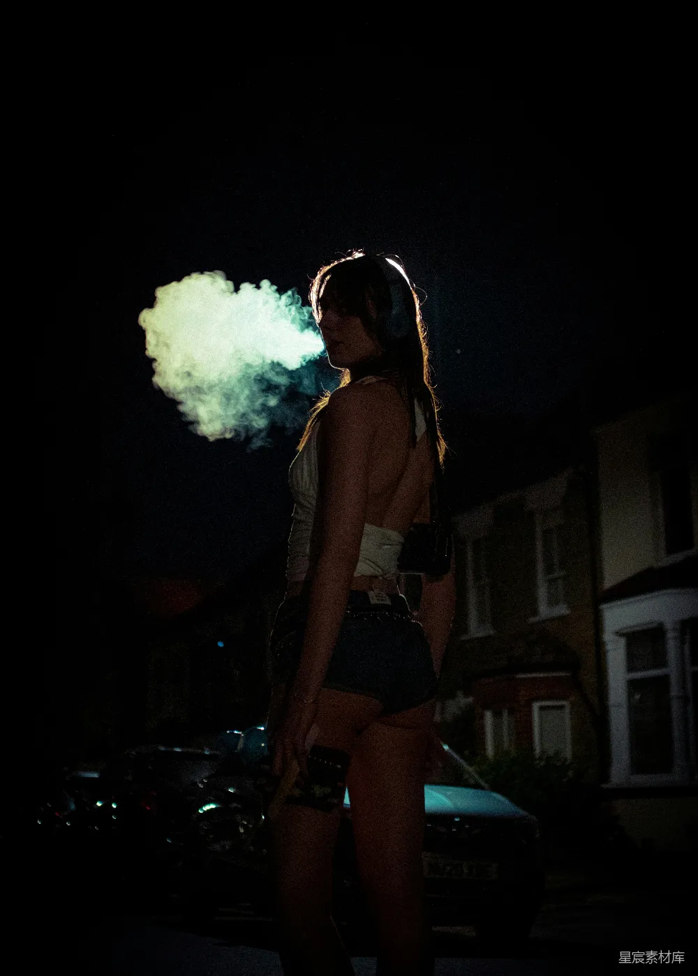 戴着耳机的女人在黑暗街道上呼出蒸汽。