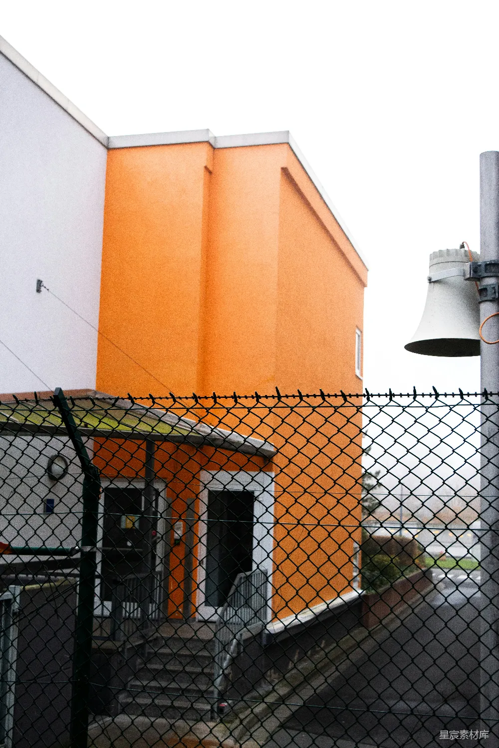 橙色建筑有白色部分和铁丝网围栏。