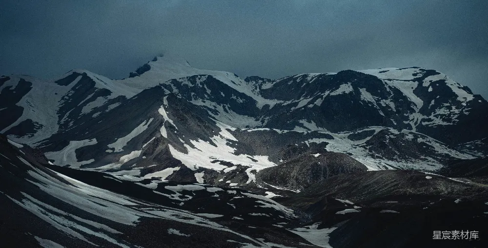 山峰被雪覆盖，在阴云密布的天空下