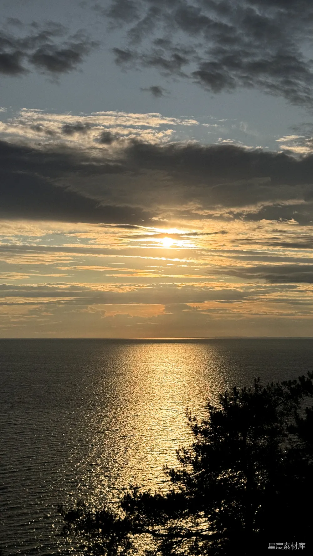 金色的夕阳映照在平静的海洋上，云朵缭绕。