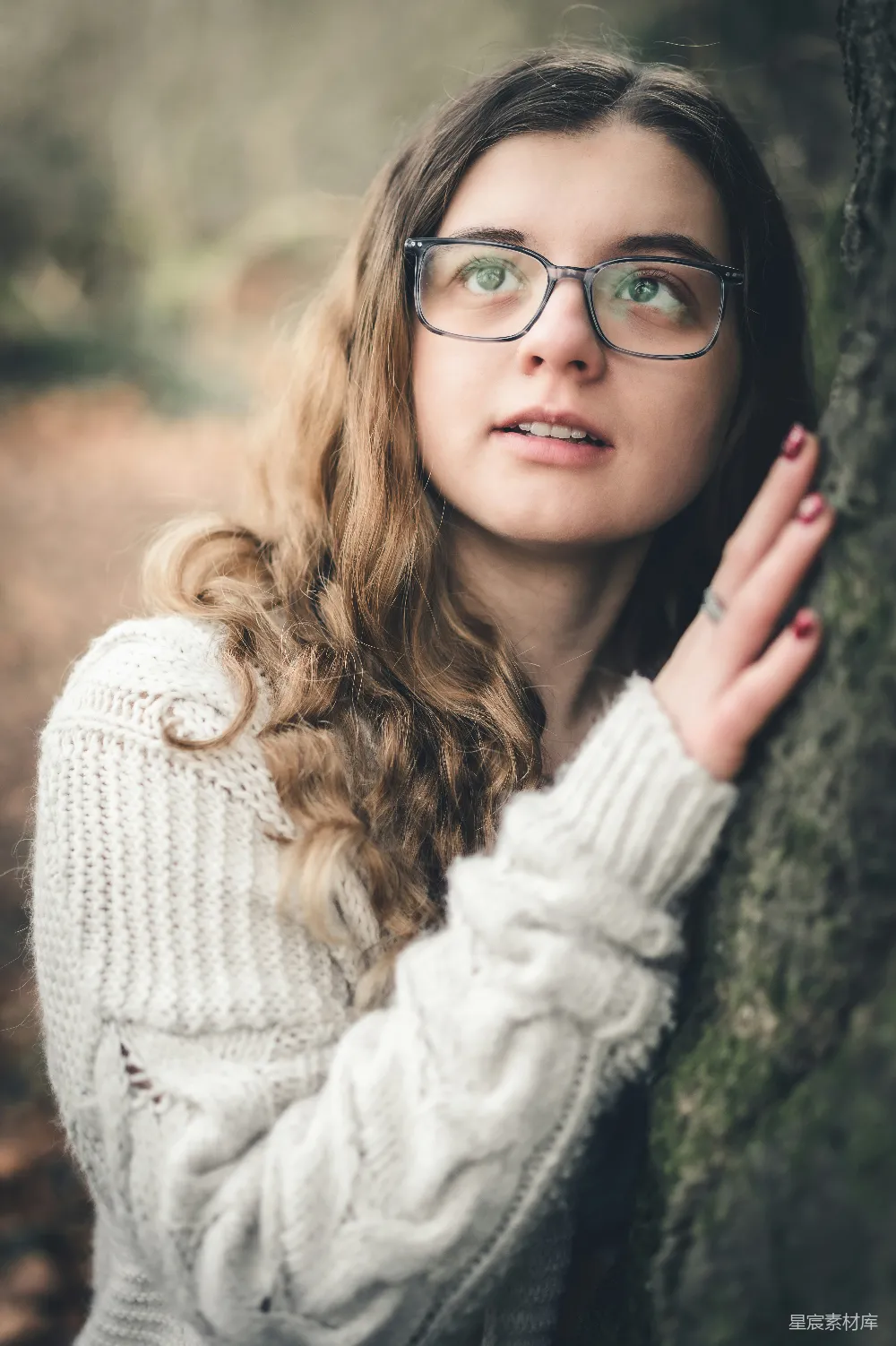 高清摄影  一个戴着眼镜的女人靠在一棵树上。