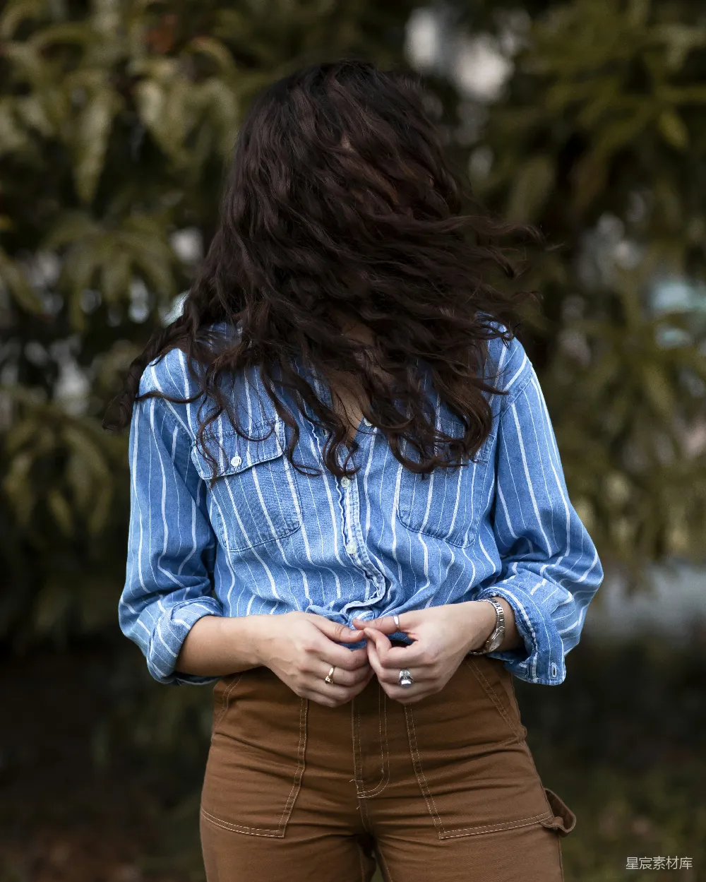 女人的脸上被他（她）的头发遮住，手里拿着一件蓝白条纹衬衫。