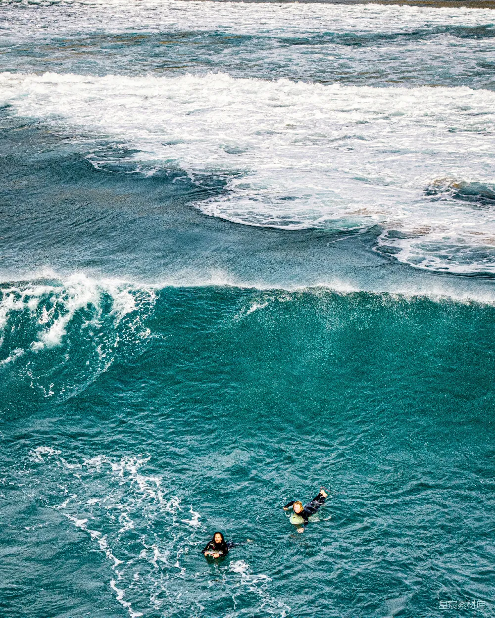 两名冲浪者在 turquoise 海洋中等待，海浪拍打着岸边。
