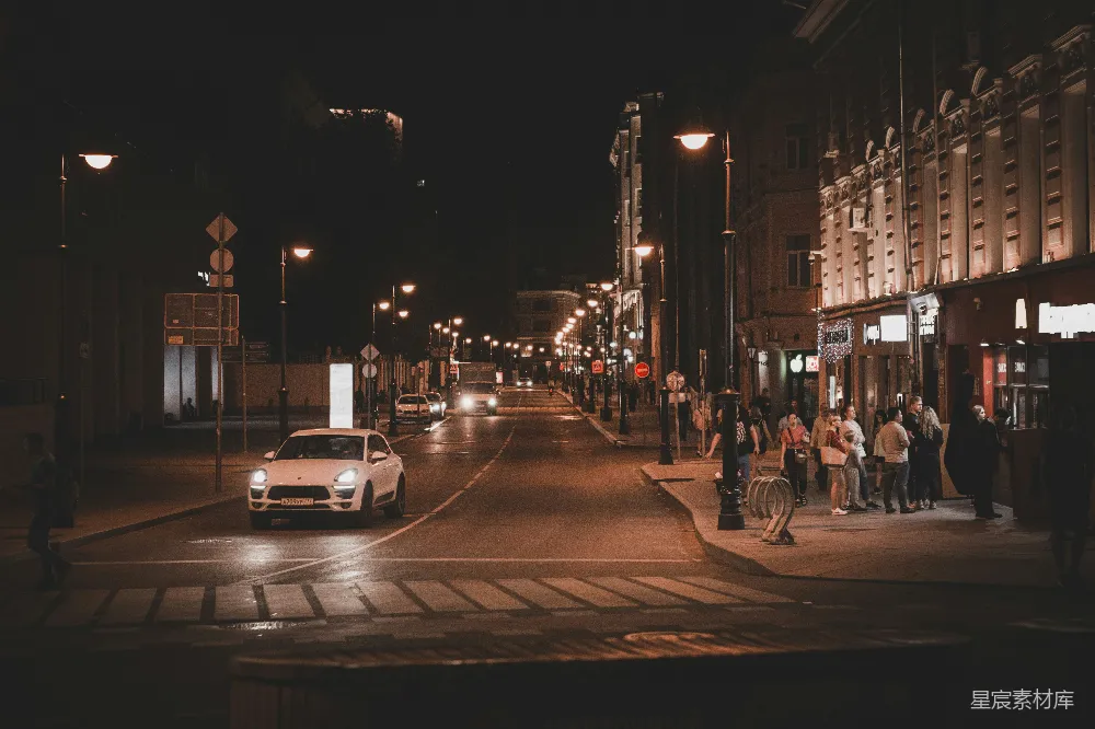 夜晚路上车辆稀少，人们在建筑物附近行走。