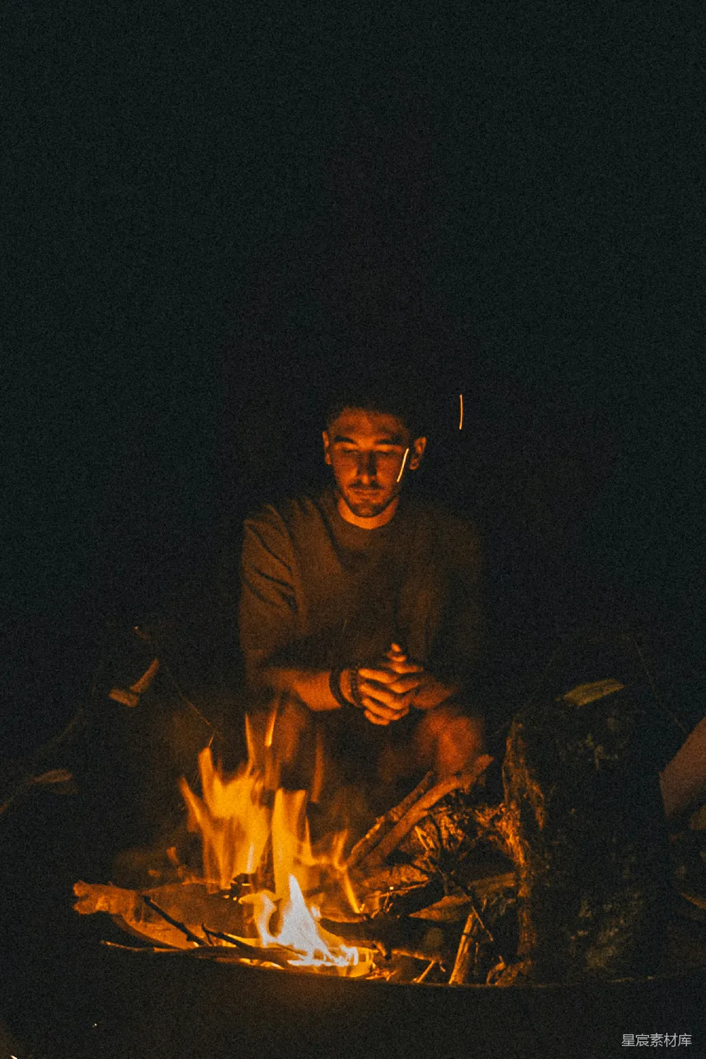 一个男人坐在篝火旁的夜间。