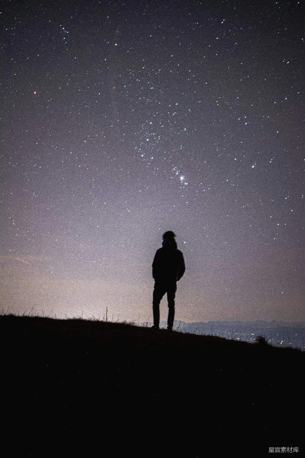 山上有人站立眺望夜空中的星星。