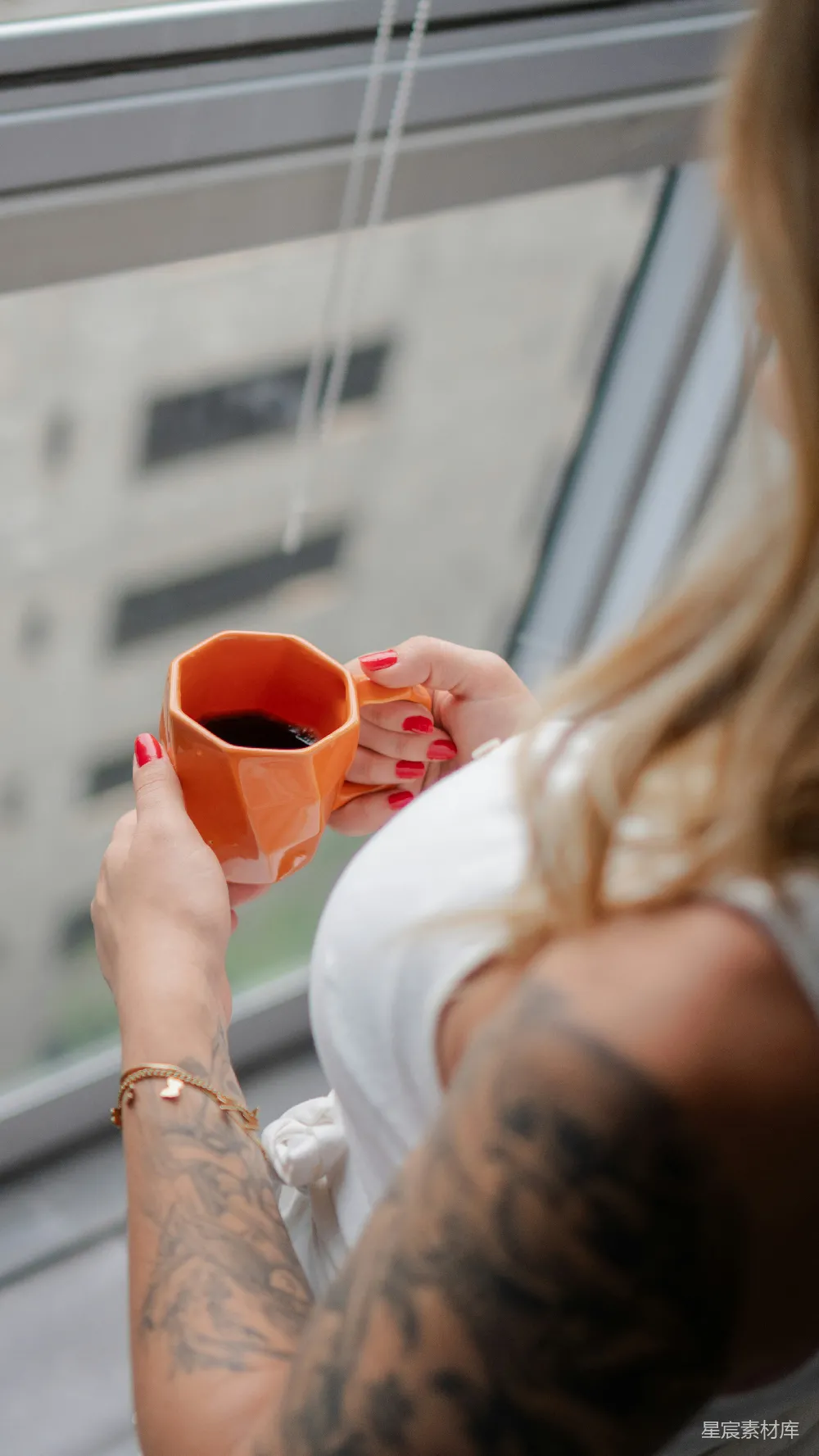 窗边的女人拿着一个橙色的咖啡杯