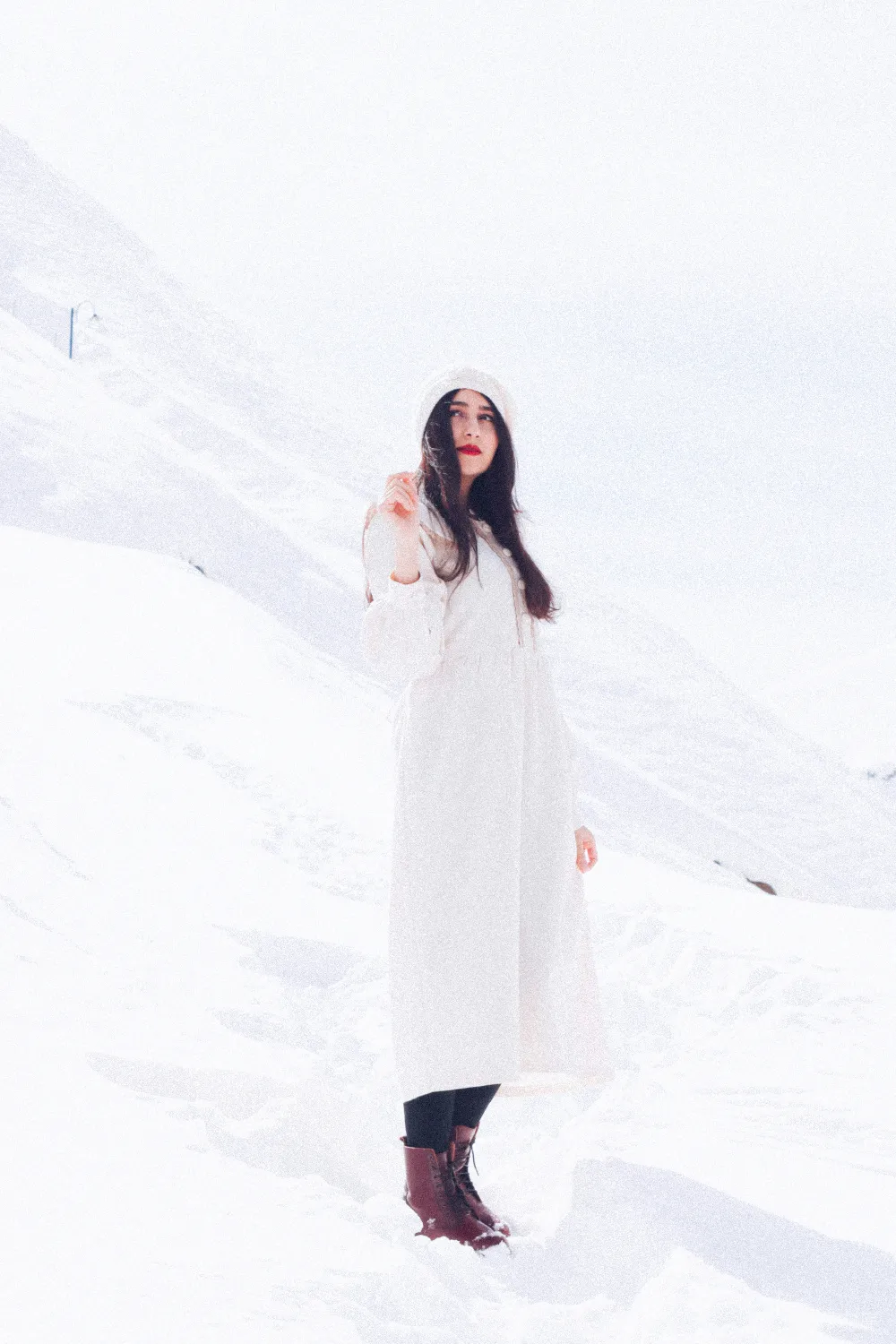 一个女人站在雪地里穿着白色风衣。