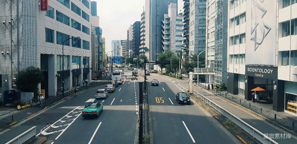 路旁近高楼的汽车在白天行驶。