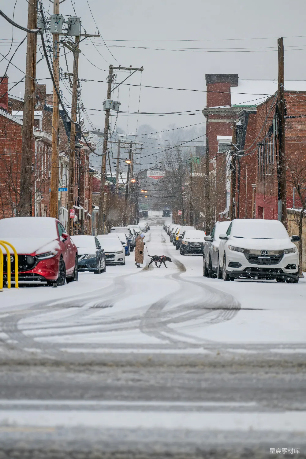 一条铺满白雪的街道，两侧停着汽车。