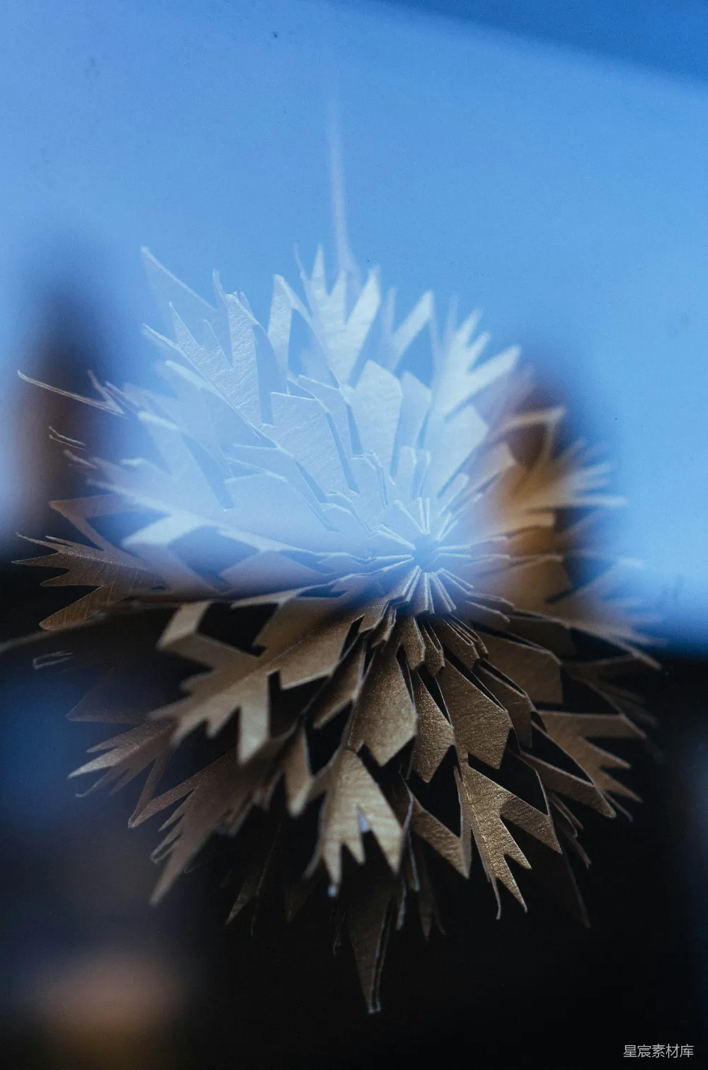 高清摄影  一张纸制雪花装饰品悬挂在蓝色背景前。