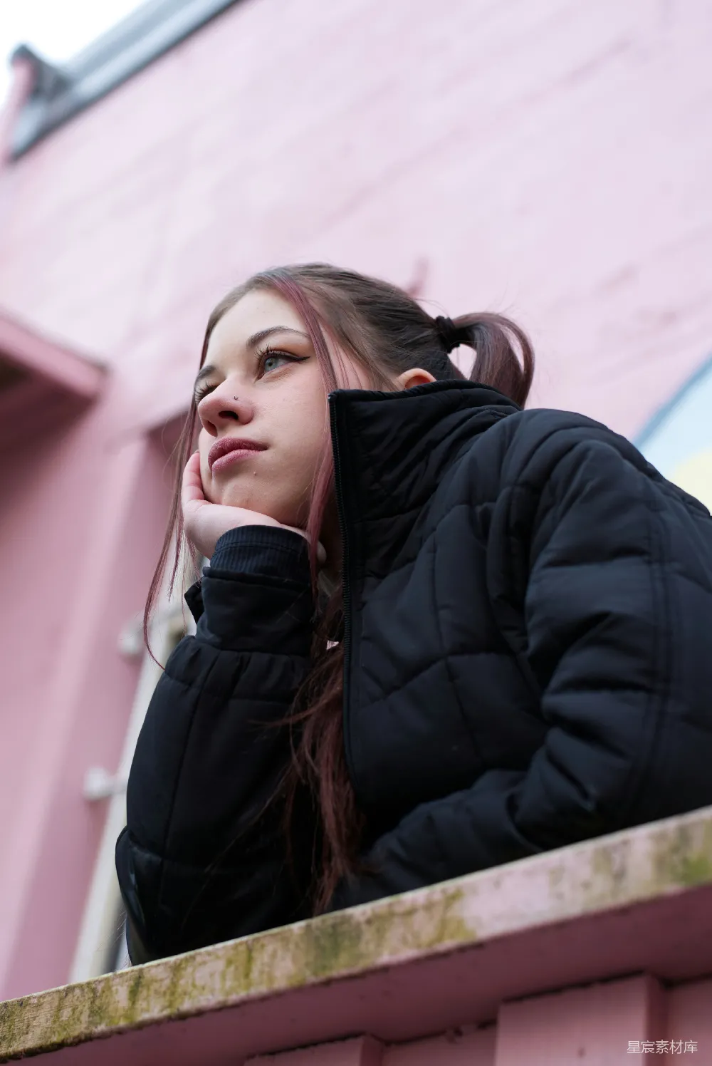 一个女人坐在粉红色的墙上。