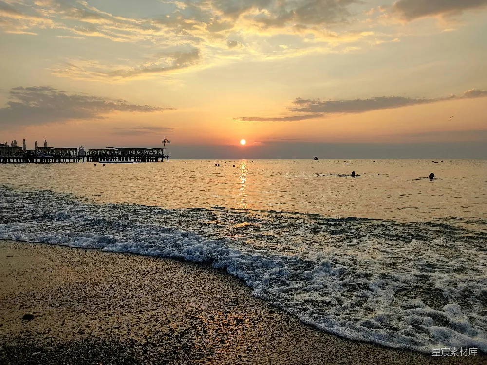 海边日落，人们在水中游泳