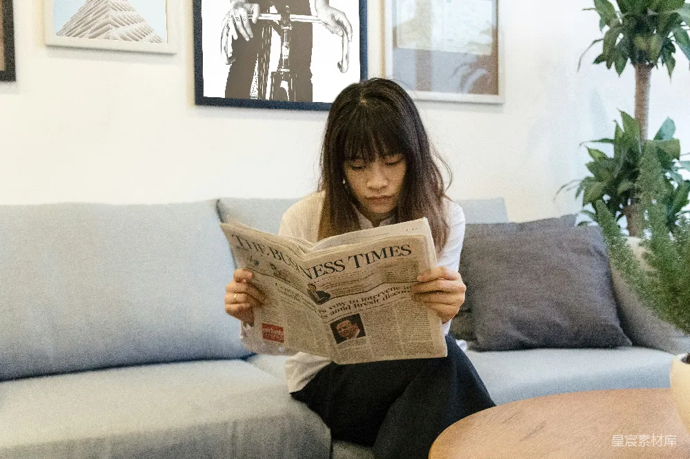 高清摄影  一个女人坐在沙发上读报纸。