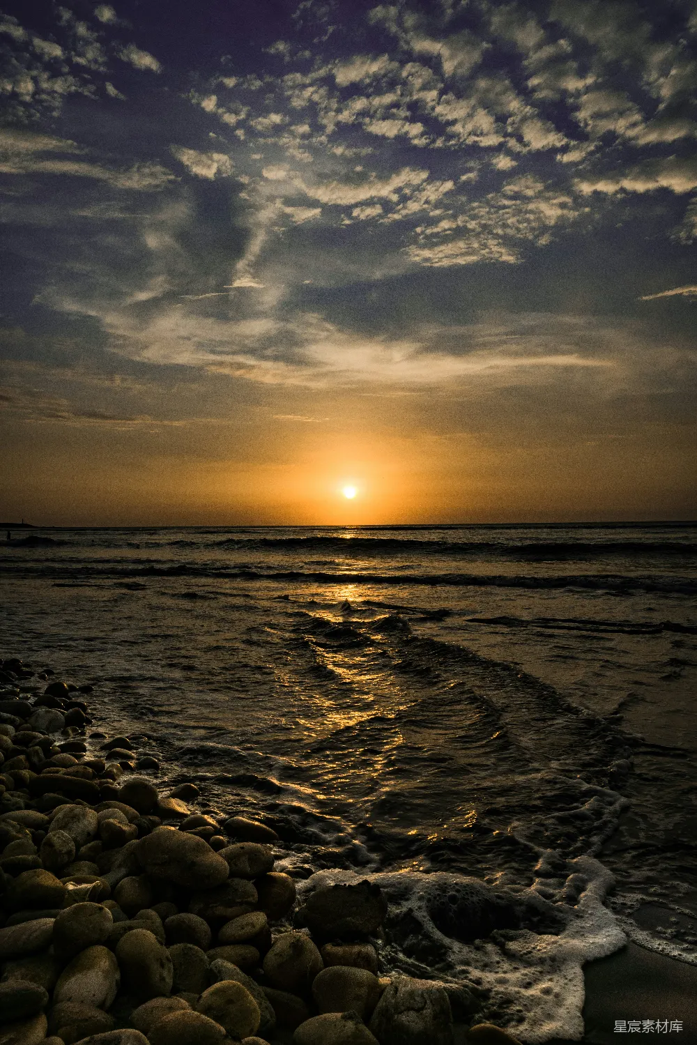 高清摄影  夕阳正在海面上落下，前景中有一些岩石。