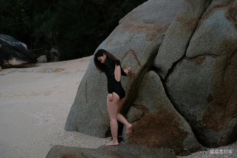 一个穿泳衣的女人站在一块大石头旁边