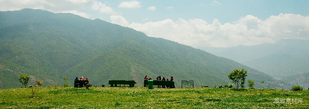 人们聚集在一片草坡上，背景是山峦。