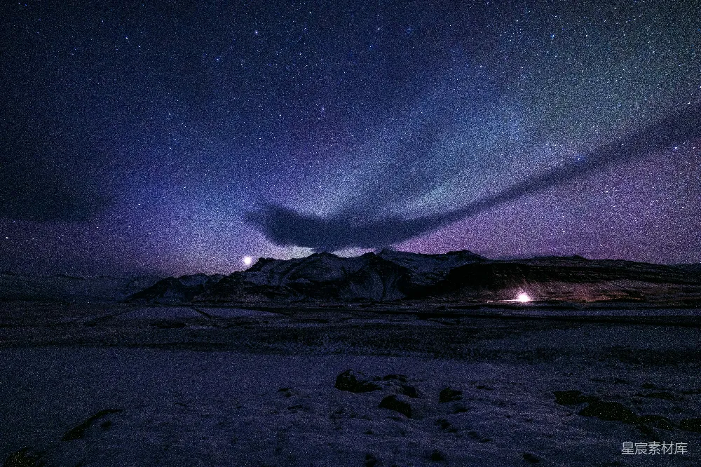 北极光照亮一片繁星满天的雪山之顶。