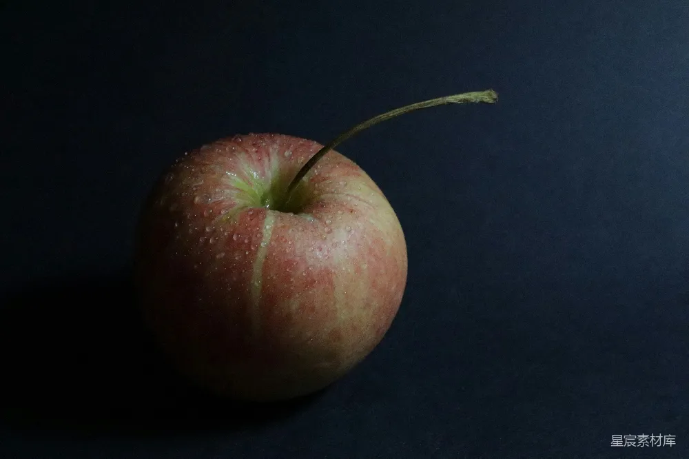 一只红苹果摆在黑色桌子的上面。