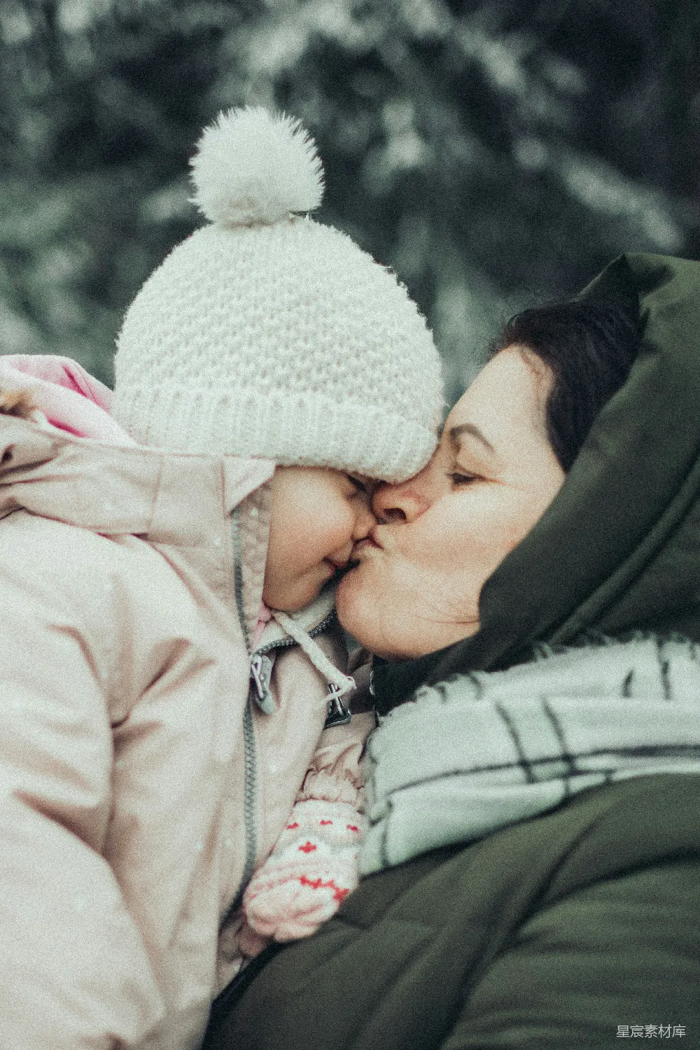 一个女人在雪中亲吻一个小孩子。